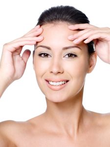 Happy smiling young beautiful woman touching her forehead without wrinkles - close-up