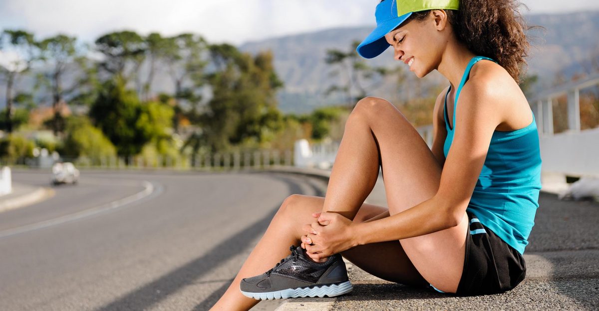 Woman sitting on the ground holding her ankle in pain