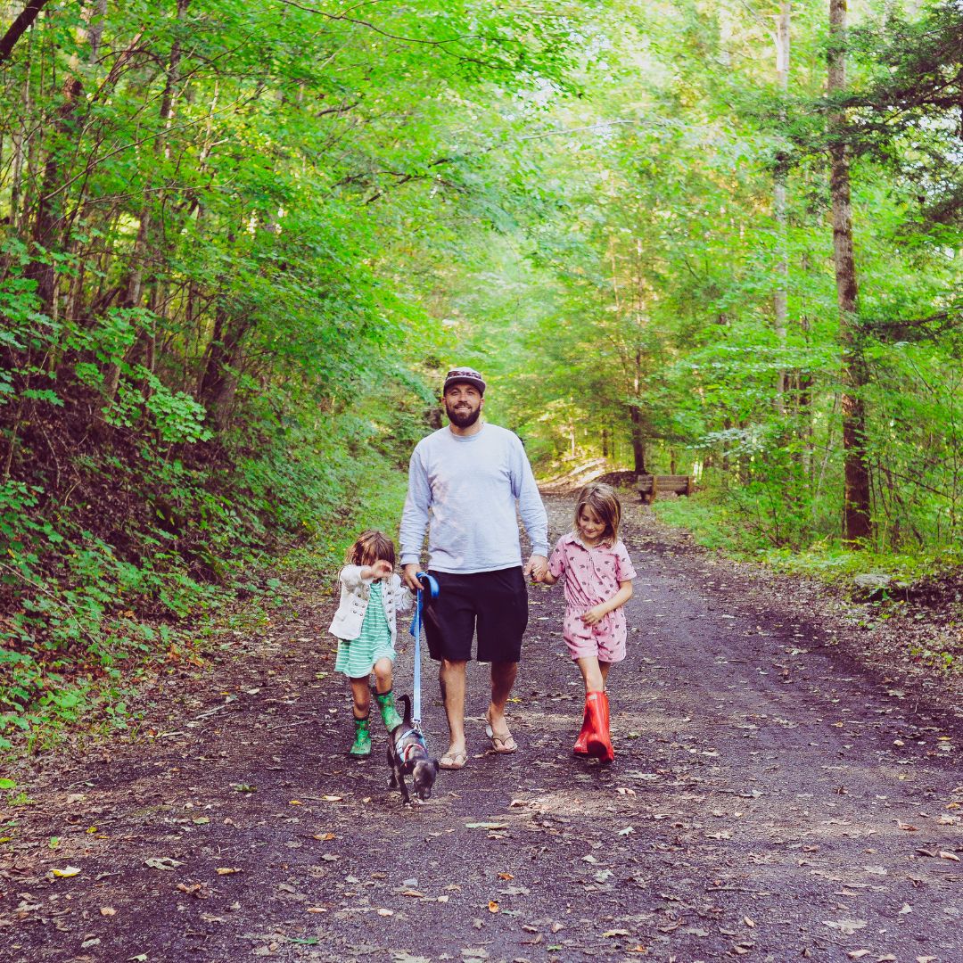 a father taking a walk on a trail with his kids and dog