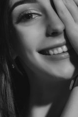 A black and white close up photo of a woman smiling with one hand resting on her face. Photo by Alexander Krivitskiy on Unsplash.