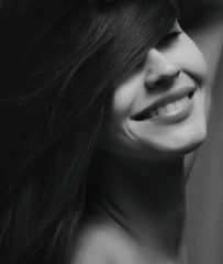 A grayscale photo of a dark haired woman smiling. Photo by Alexander Krivitskiy on Unsplash.
