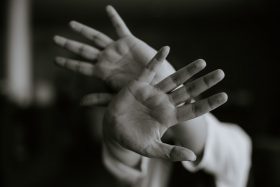 A grayscale photo of a person stretching their hands out in front of them, as if to shield themselves from a threat. Photo by M.T ElGassier on Unsplash.