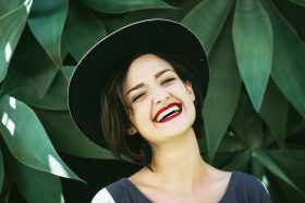 A woman smiles in front of a large green plant. Photo by Matheus Ferrero on Unsplash.