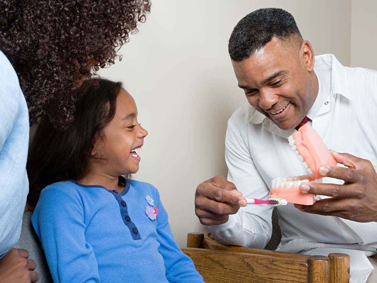 Dentist showing young girl a model of teeth with toothbrush