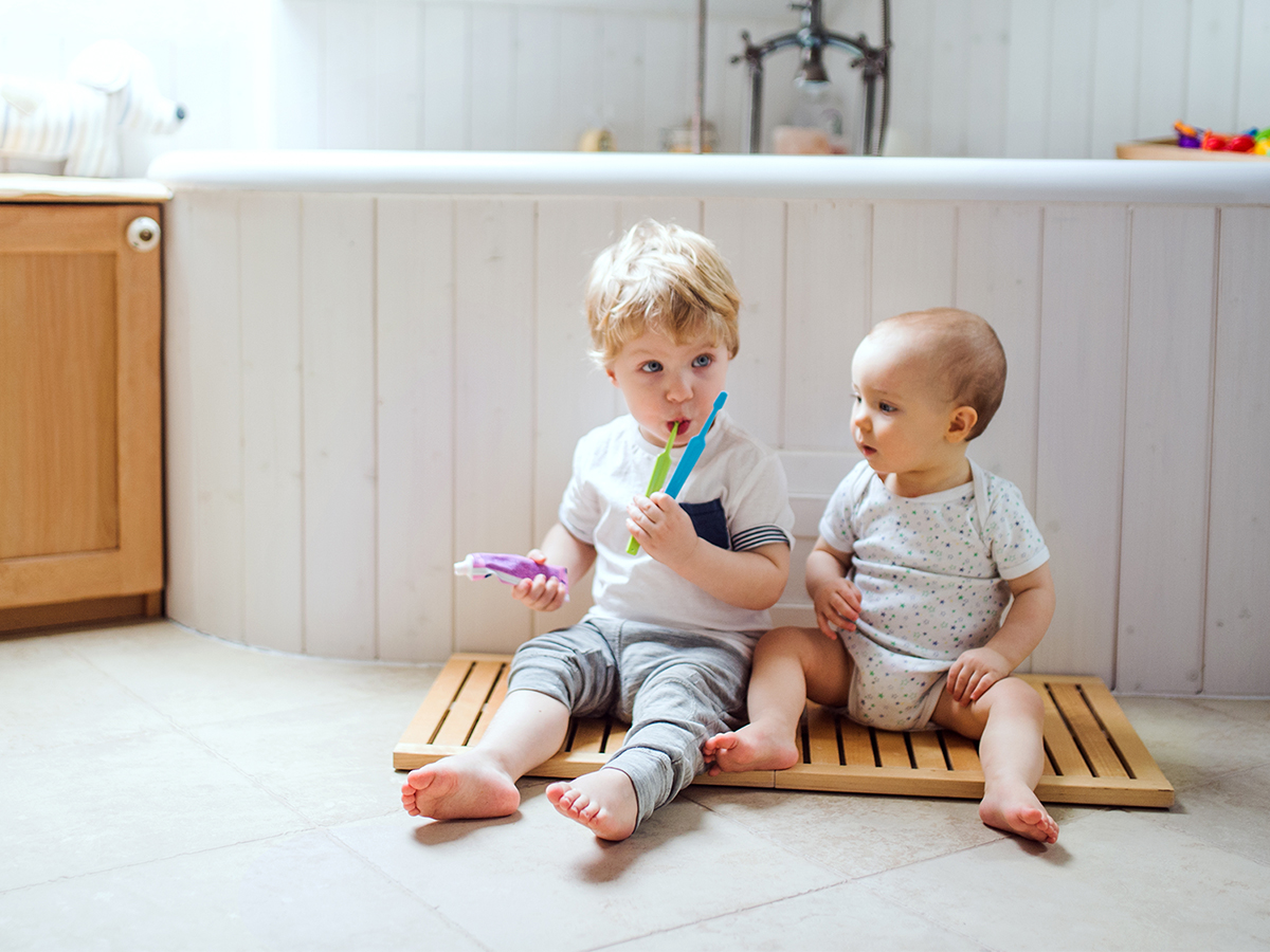 Two toddler children sitting on the floor and brushing teeth in the bathroom at home