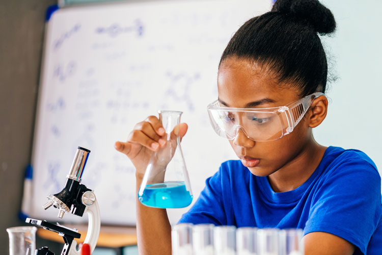 Indy STEAM Academy student wearing goggles with beaker and microscope