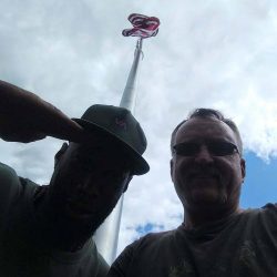 Two guys with flag pole above them, saluting - ND Flag Pole Guy