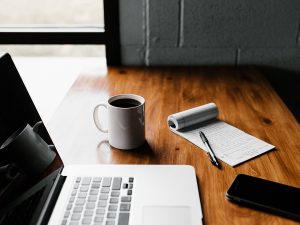 A laptop, notepad, and cup of coffee.