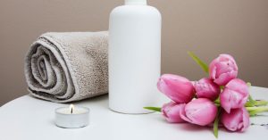 Rolled up towel, lit candle, pink flowers, and a cleanser.