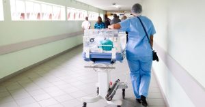 Person in scrubs in a medical setting walking down a corridor.