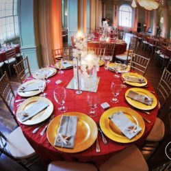A wedding reception table with red table cloth and gold accents - The Rented Event